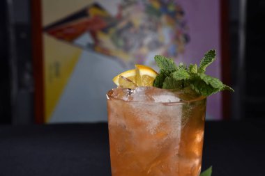 Böğürtlenli, buzlu ve cinle ferahlatıcı alkollü içecek, arka planda bulanık duran cam bardakta servis edilen limon kabuğu.