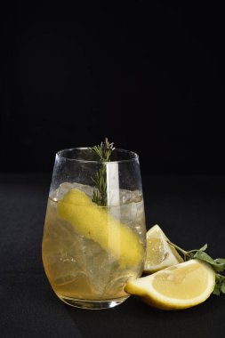 Böğürtlenli, buzlu ve cinle ferahlatıcı alkollü içecek, arka planda bulanık duran cam bardakta servis edilen limon kabuğu.