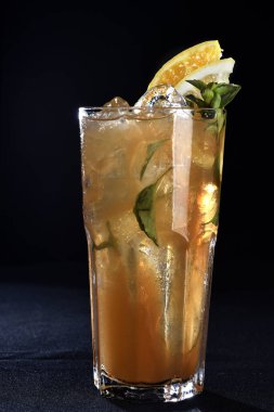 Böğürtlenli, buzlu ve cinle ferahlatıcı alkollü içecek, arka planda bulanık duran cam bardakta servis edilen limon kabuğu.