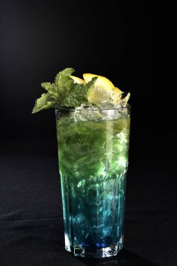 Böğürtlenli, buzlu ve cinle ferahlatıcı alkollü içecek, arka planda bulanık duran cam bardakta servis edilen limon kabuğu.