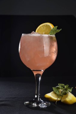 Böğürtlenli, buzlu ve cinle ferahlatıcı alkollü içecek, arka planda bulanık duran cam bardakta servis edilen limon kabuğu.