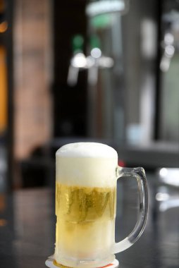 Enfes soğuk ve ferahlatıcı bira kupası bulanık arka planda masanın üstünde.