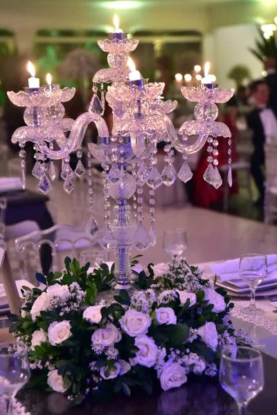 A luxurious bouquet of fresh flowers in a crystal vase on the table with cutlery plates and an elegant portion in the party restaurant with backlit and unfocused background.