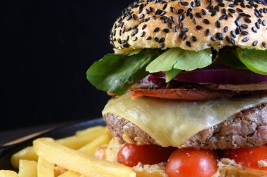 Peynirli, salatalı, turşulu ve siyah arka planda izole edilmiş susamlı burger..