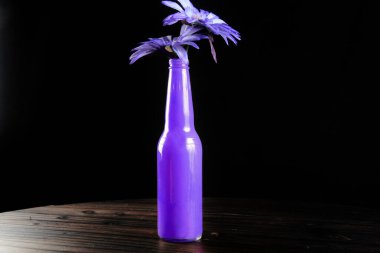 Siyah arka planda mavi çiçekli mor şişe.