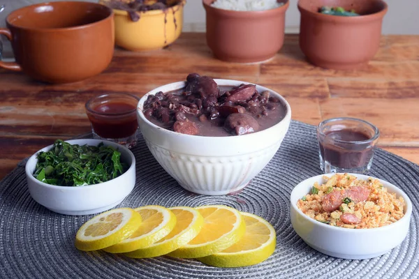 l Brazilian food feijoada made with beans, pork, bacon, sausage with cabbage, rice, salad, spices and pepper.