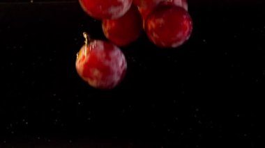 Hava kabarcıklarıyla suya düşen bir üzüm. Siyah bir arkaplanda.