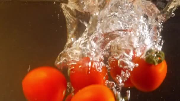 Κόκκινα ντοματίνια πέφτουν στο νερό με φυσαλίδες αέρα. Μαύρο φόντο. Αργή κίνηση — Αρχείο Βίντεο