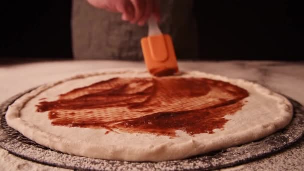 Pizza maken in de keuken. close-up op chef-kok zetten tomatensaus op pizza — Stockvideo