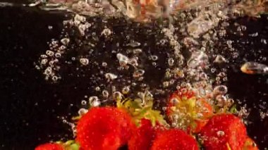 Suda yüzen çileklerin detaylı çekimi. Renkli böğürtlenler yavaş çekimde sıvıya batıyor. 