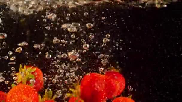 Sparatoria dettagliata di fragole che galleggiano in acqua. Bacche colorate che affondano nel liquido al rallentatore. — Video Stock