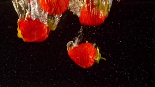 Λεπτομερής λήψη φραουλών που επιπλέουν στο νερό. Πολύχρωμα μούρα που βυθίζονται στο υγρό σε αργή κίνηση. — Αρχείο Βίντεο
