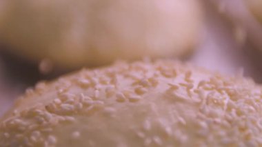 Beyaz susam tohumları ağır çekimde hamburgerlerin üzerine düşer.