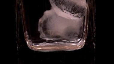 Buz, temiz, boş bir malt bardağa düşer. Cam siyah bir standın üzerinde.. 