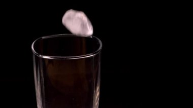 Buz, temiz, boş bir malt bardağa düşer. Cam siyah bir standın üzerinde.. 
