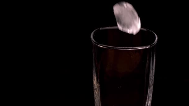 La glace tombe dans un verre simple malt clair et vide. Le verre est sur un support noir. — Video