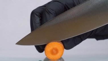 Bıçakla havuç kesmek. Siyah eldivenli şef havucu yuvarlak parçalara ayırdı.. 