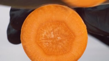 Havucu bıçakla keserken yakın plan. Siyah eldivenli şef havucu yuvarlak parçalara ayırdı. 