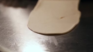 Baker fırın mutfağında merdaneyle hamur topluyor. Erkeklerin elleri hamuru dışarı atıyor. Erkek elleri çelik mutfak masasında hamuru yuvarlıyor..