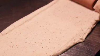 Aşçı aşçı hamuru çelik mutfak masasında merdaneyle yuvarlıyor. Erkek eli hamuru merdaneyle çevirir.