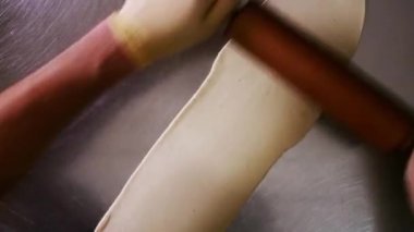 Şef mutfak masasında merdaneyle hamuru yuvarlıyor. Erkek eli hamuru rulo pin pişirme pizzası kullanarak yuvarlıyor. Erkek elleri metal masada hamuru yuvarlıyor.
