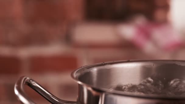 Water boiling in steel pot. Bubbles of boiling water. Male hand close saucepan cover. Slow motion shot. — Stock Video
