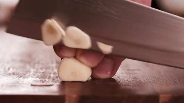 Mann schneidet in Zeitlupe Knoblauchzehen auf Holzbrett mit Stahlmesser. — Stockvideo