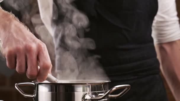 Шеф-повар в черном фартуке готовит макароны из кипящей воды. Белый дым в замедленной съемке поднимается над горячей кастрюлей. Готовить дома. Вкусная итальянская паста. — стоковое видео