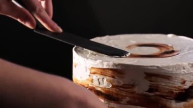 Şefin elleri çikolatalı kekin üzerine krema sürüyor. Katmanlı çikolatalı pasta