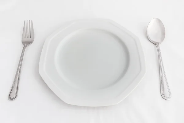 Assiette blanche, cuillère et fourchette sur fond blanc . — Photo