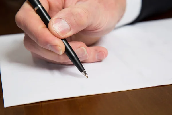 Mano de un hombre de negocios sosteniendo una pluma sobre un papel — Foto de Stock