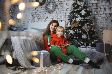 Kırmızı, sıcak kazaklı kızı olan anne yatakta zıplıyor. Mutlu annelikler. Sıcak aile ilişkileri. Noel ve Yeni Yıl arifesi. Sevgi. Aile kavramı.