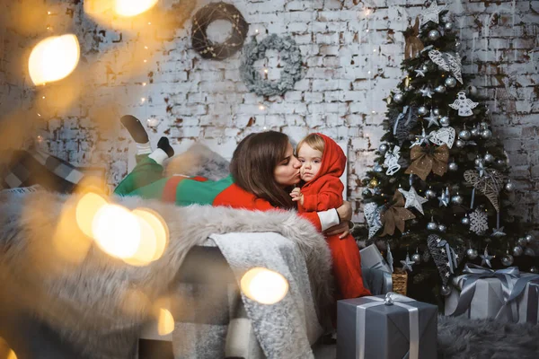 Mom with daughter in red warm sweaters are jumping on the bed. Happy motherhood. Warm family relationships. Christmas and New Year\'s interior. Love. Family concept.