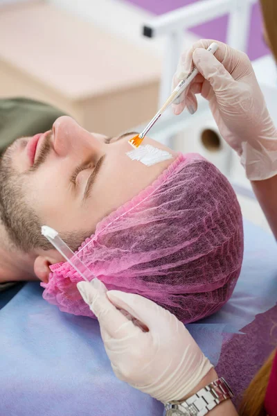 Kosmetolog Nakłada Białą Maskę Nawilżającą Twarz Człowieka Pomocą Pędzla Klinice — Zdjęcie stockowe