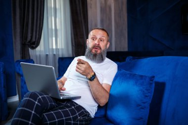 Yetişkin bir erkek işadamı yeni bir proje üzerinde çalışıyor ve hisse senedi büyüme grafiklerine bakıyor. Büyük pencerenin yanındaki masada oturuyor. Dizüstü bilgisayara bakar