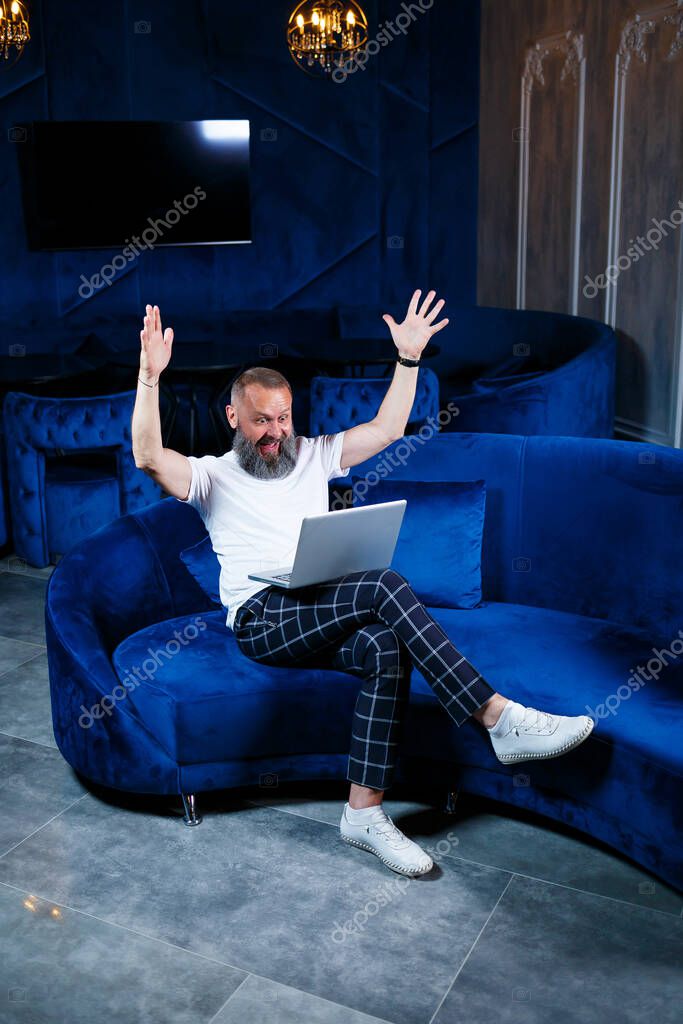 An adult male businessman is working on a new project and looking at the stock growth charts. Sits at the table by the large window. Looks at laptop screen