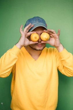 Kafasında kep olan sakallı, yeşil arka planda limonları olan genç bir adam. Sarı kazaklı bir adamın portresi.