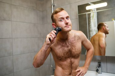Bir adam aynanın önünde yüzünü jiletle traş eder. Deri tahrişi. Banyo prosedürü
