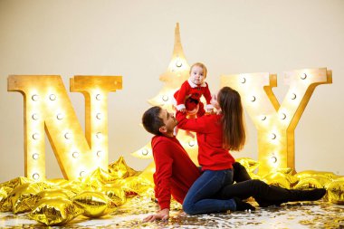 Kırmızı kazaklı mutlu bir aile yerde birlikte oturuyor. Noel tatili atmosferi. Noel Baba kostümü giymiş bir çocuk. Aile ilişkisi kavramı