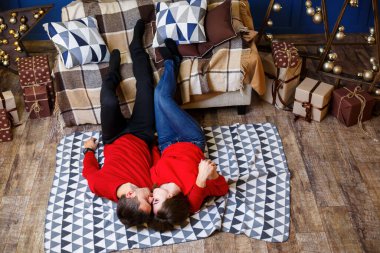 Romantik bir an. Kırmızı kazaklı bir çift yerde uzanıyor ve sarılıp öpüşüyor.