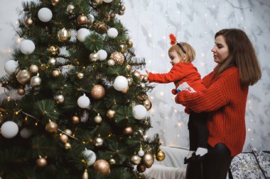 Kırmızı süveter giyen anne ve kız Noel ağacını süslüyor. Mutlu annelikler. Sıcak aile ilişkileri. Noel ve Yeni Yıl arifesi. Sevgi. Aile kavramı.