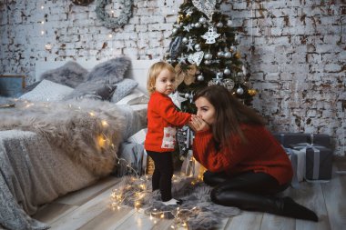 Kırmızı, sıcak kazaklı kızı olan anne yatakta zıplıyor. Mutlu annelikler. Sıcak aile ilişkileri. Noel ve Yeni Yıl arifesi. Sevgi. Aile kavramı.