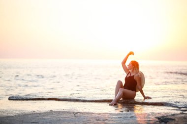 Deniz kıyısında siyah mayolu güzel bir bayan omuzlarında hasır bir şapkayla gülümseyen bir yüz. Altın günbatımı ışığı