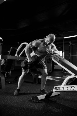 Vücut geliştirme egzersizinin bir parçası olarak kaslı üstsüz bir adam dambıl egzersizi yapıyor. Fitness motivasyonu, spor yaşam tarzı, sağlık, atletik vücut, vücut pozitifliği