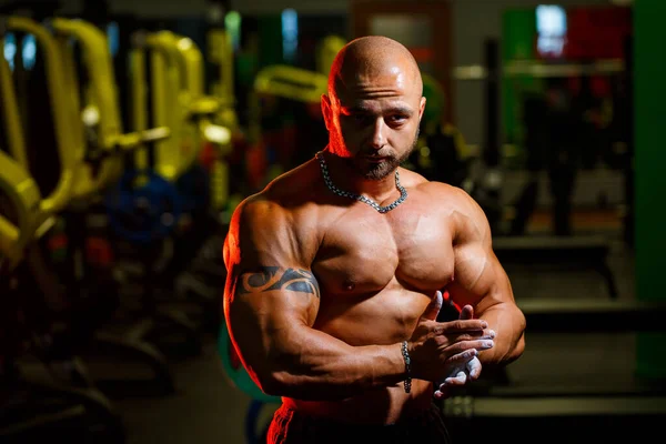 Sporty handsome strong man posing on the background of the gym. A strong bodybuilder with perfect abs, shoulders, biceps, triceps and chest.