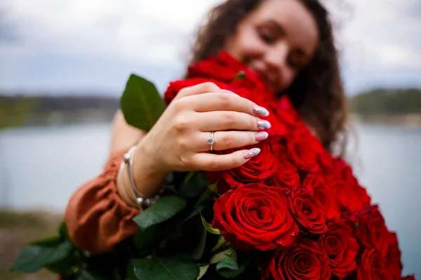 红玫瑰花束上的一个戴着结婚戒指的女孩的手 — 图库照片