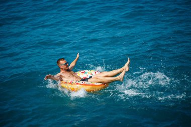 Genç bir adam güneşli bir günde şişme bir yüzükle açık denizde yüzer. Yaz tatili, tatildeki turist.