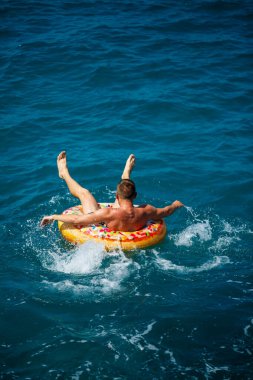 Genç bir adam mavi suyla denizde şişirilebilir bir halka üzerinde yüzüyor. Güneşli bir günde güzel bir tatil. Tatil konsepti, üst görünüm.