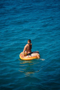 Genç bir adam mavi suyla denizde şişirilebilir bir halka üzerinde yüzüyor. Güneşli bir günde güzel bir tatil. Tatil konsepti, üst görünüm.