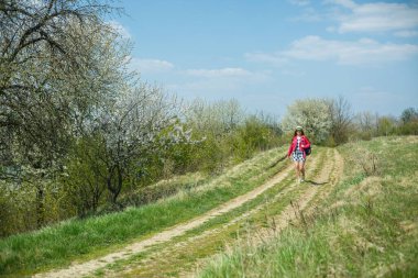 Ağaçların çiçek açtığı bahar ormanında yürüyen elbiseli güzel bir kız.